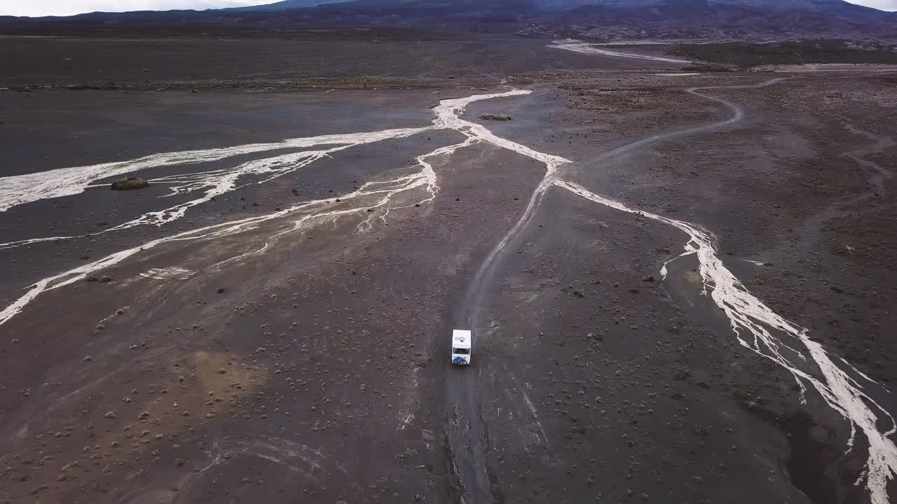 An old camper van drives trough the desert at Tukino Access Road. a dry river is on the way through Tongariro National Park - Rangipo Desert.