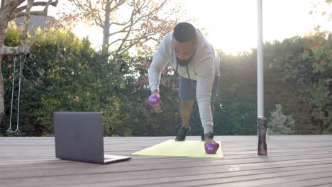 African-american-man-fitness-training-exercising-with-weights-on-deck-in-sunny-garden,-slow-motion