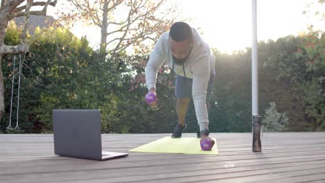 african american man fitness training exercising with weights on deck in sunny garden, slow motion