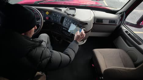 typical-american-truck-driver-using-google-maps-seating-on-driver-sit-in-a-red-cascadia-volvo-truck-and-browsing