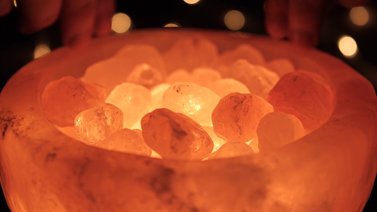 Mani di persona sopra una lampada a ciotola di sale rosa arancione luminoso
