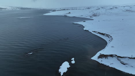 small waves on a calm sea roll out on the snowy coast of iceland during a light snowfall