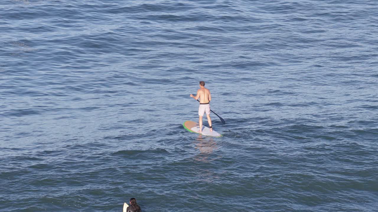 Aerial view of a stand-up paddleboarder navigating rough sea waves on the Gold Coast, Australia, under clear skies