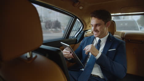 un profesional de sexo masculino sonriente leyendo buenas noticias en una tableta en un automóvil.