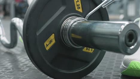 close up of person clipping weight plate onto bar with foot and leg visible in gym group on rubber floor, showcasing hands securing metal spring collar on chrome bar end during workout prep
