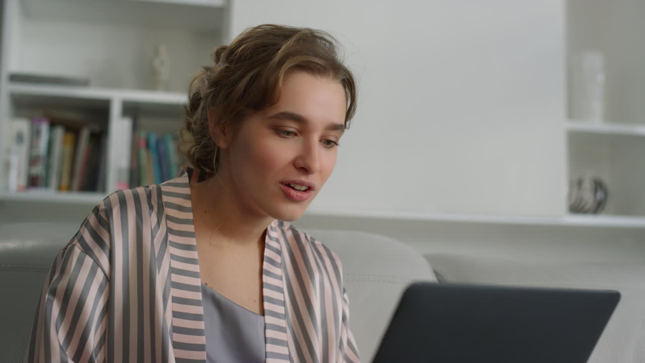 Nærbillede af overrasket kvinde, der taler i videokonference med en veninde hjemme i tøj