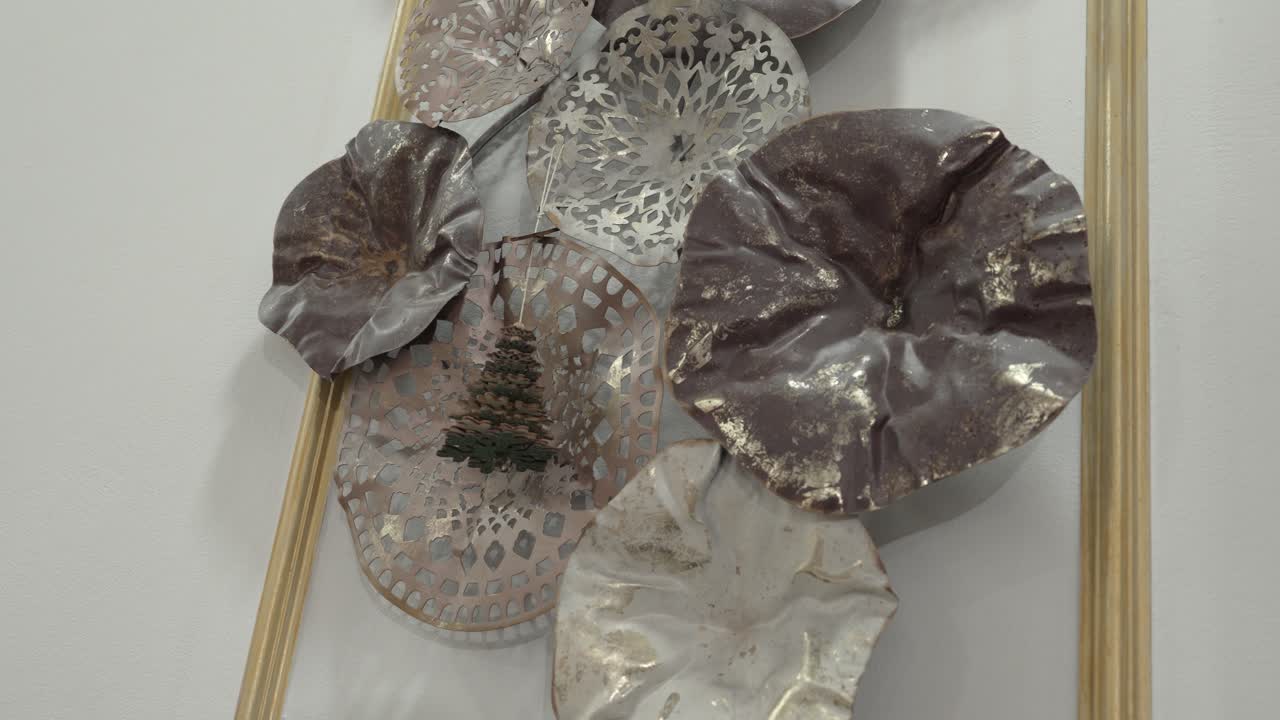 Kolekce unikátních kovových dekorací je vystavena na zdi. Expozice obsahuje různé tvary a textury. Některé dekorace mají složité vzory.
