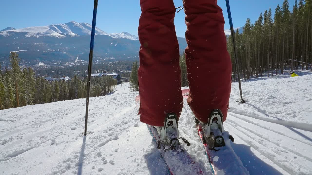 bajo ángulo de esquiador clipping en un par de esquís y comienza a empujar hacia abajo de la montaña hacia una estación de esquí en cámara lenta