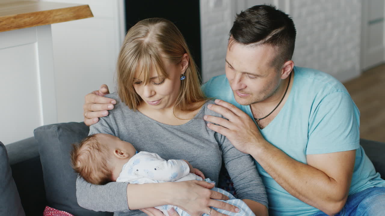 아기를 안고 집에서 쉬고 있는 젊은 부부