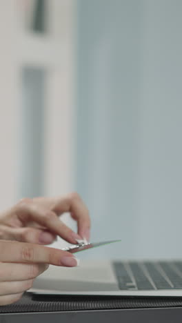 woman enters credit card details on website of online shop via modern laptop on blurred background. housewife makes payment sitting at table closeup