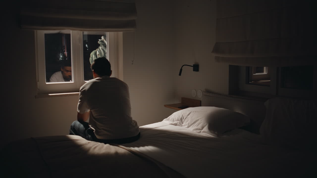 Silhouette sad man sitting bed home looking window feeling lonely. Guy insomnia