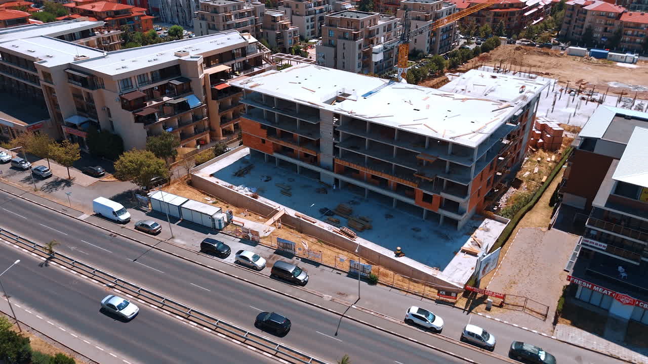 Varna, Bulgaria, 29 June 2025: Close aerial view of construction next to a highway. The unfinished building is situated directly next to a busy road with traffic and parked vehicles