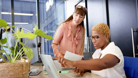 collaborating in office, two women discussing documents at desk with laptop