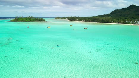 Pareja-Remando-En-La-Laguna-Muri-En-Rarotonga-Durante-La-Marea-Alta-Con-Montañas-Al-Fondo