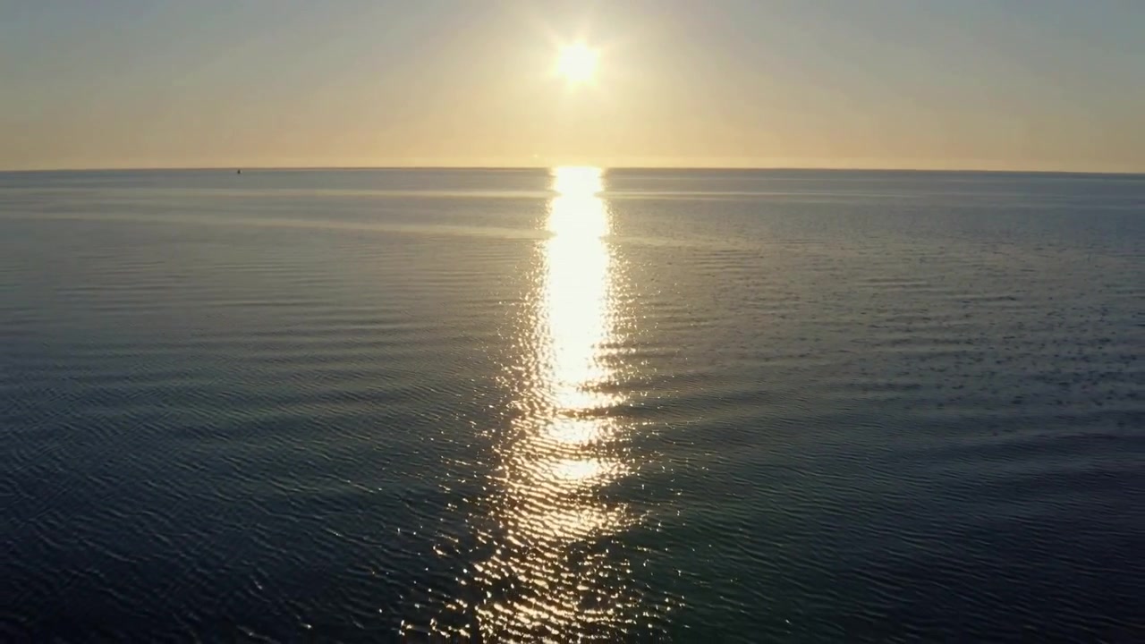Solen nærmer sig horisonten og kaster lodret refleksion på åbent hav, små bølger kruser, bøje til venstre