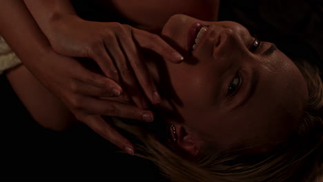 portrait of an attractive woman lying in a dark bedroom and sensually caressing her face while smiling enticingly