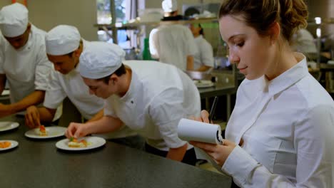 Female-chef-writing-on-notepad-in-kitchen-4k