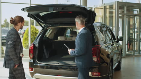 car salesman showing a car trunk to a customer