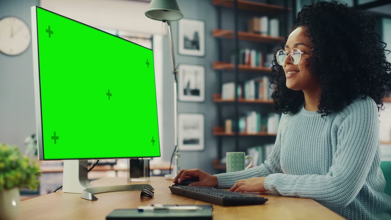 Latina Female Specialist Working on Desktop Computer with Green Screen Mock Up Display at Home Living Room while Sitting at a Table. Freelancer Female Chatting Over the Internet on Social Networks.