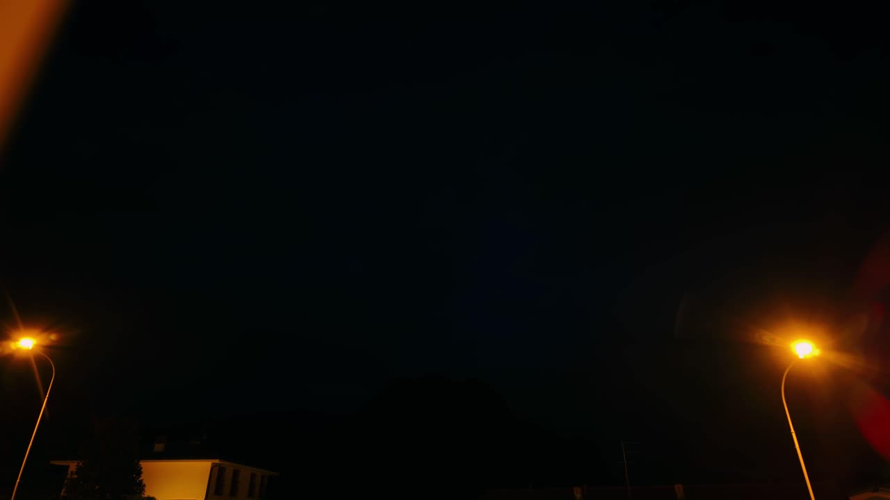 Night time lapse showing dark clouds moving over mountains and street lights in Riva di Solto Italy. Cinematic evening sky transition with illuminated street lamps and mountain silhouette