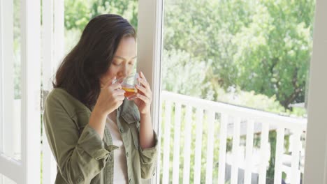 Happy-asian-woman-drinking-tea-and-looking-through-window,-in-slow-motion