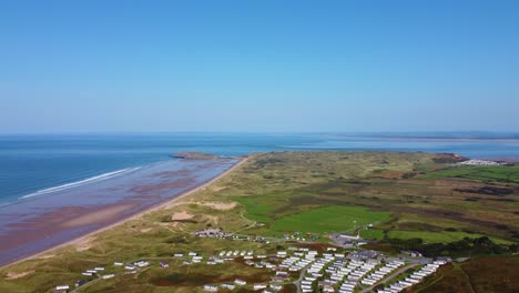 rising aerial drone shot over caravan holiday park with large beach with bright blue sea water and sprawling dunes landscape background 4k