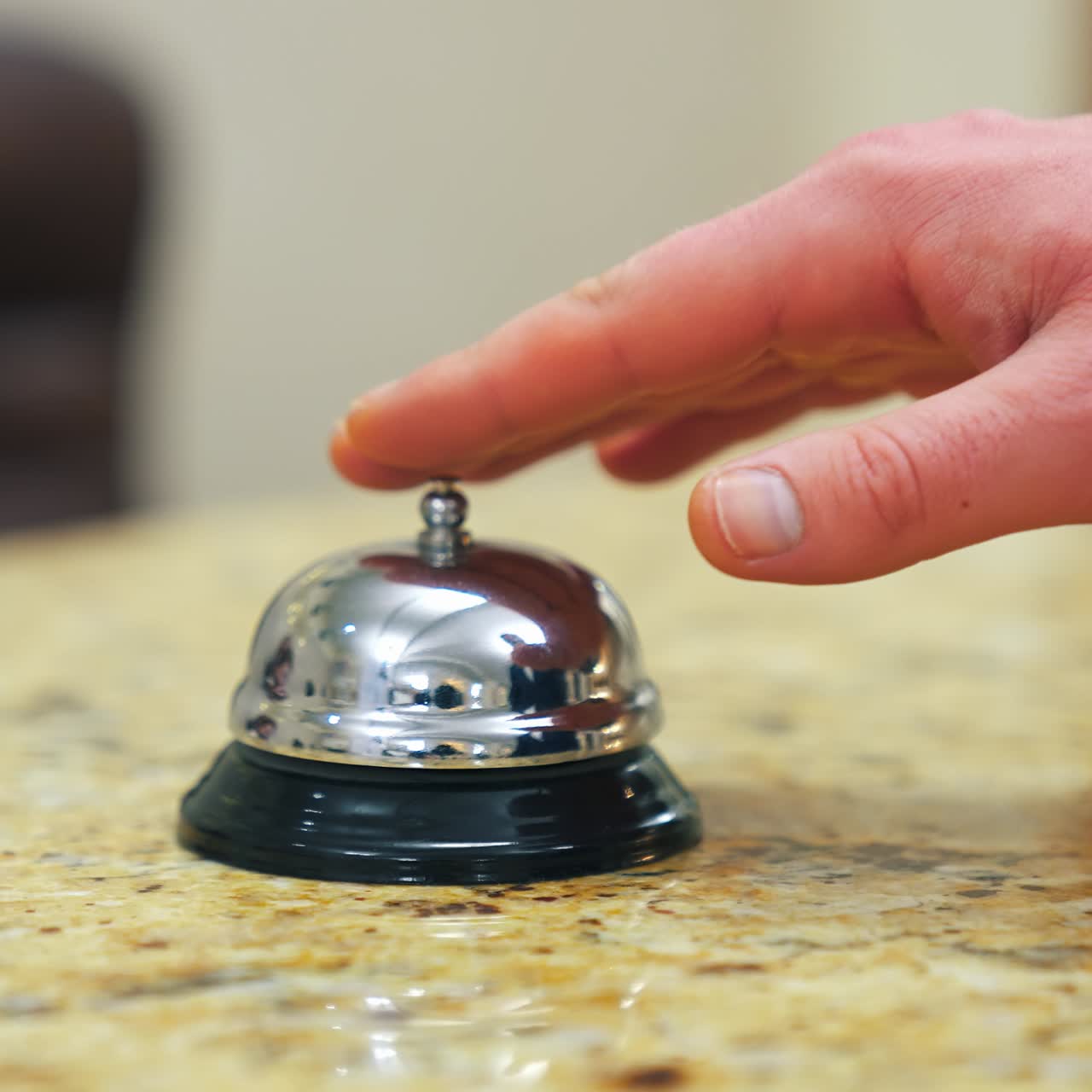Hotel bell on reception table. Man's hand presses bell button to call the receptionist in the hotel. Customer touches the metal alarm. Close-up