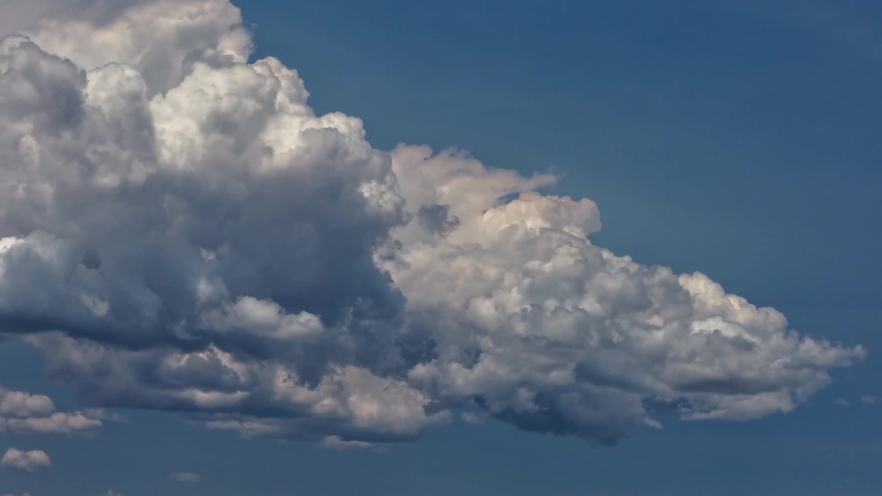4K UHD aerial timelapse featuring a tight, detailed shot of a rapidly morphing cumulus cloud. Bright white and dark grey textures shift dynamically against a crisp blue sky as the formation builds.