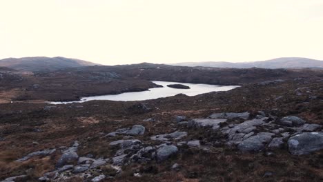 Scenic-landscape-view-of-loch-of-water-with-boulders-and-tussock-in-the-outdoor-wilderness-of-Outer-Hebrides-of-Scotland-UK