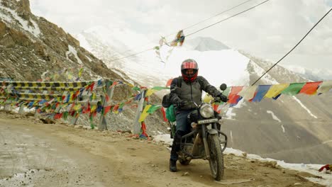 biker gets onto a snowy mountain road in ladakh, india, a high-altitude journey through rugged snow terrain with buddhist prayer flags behind
