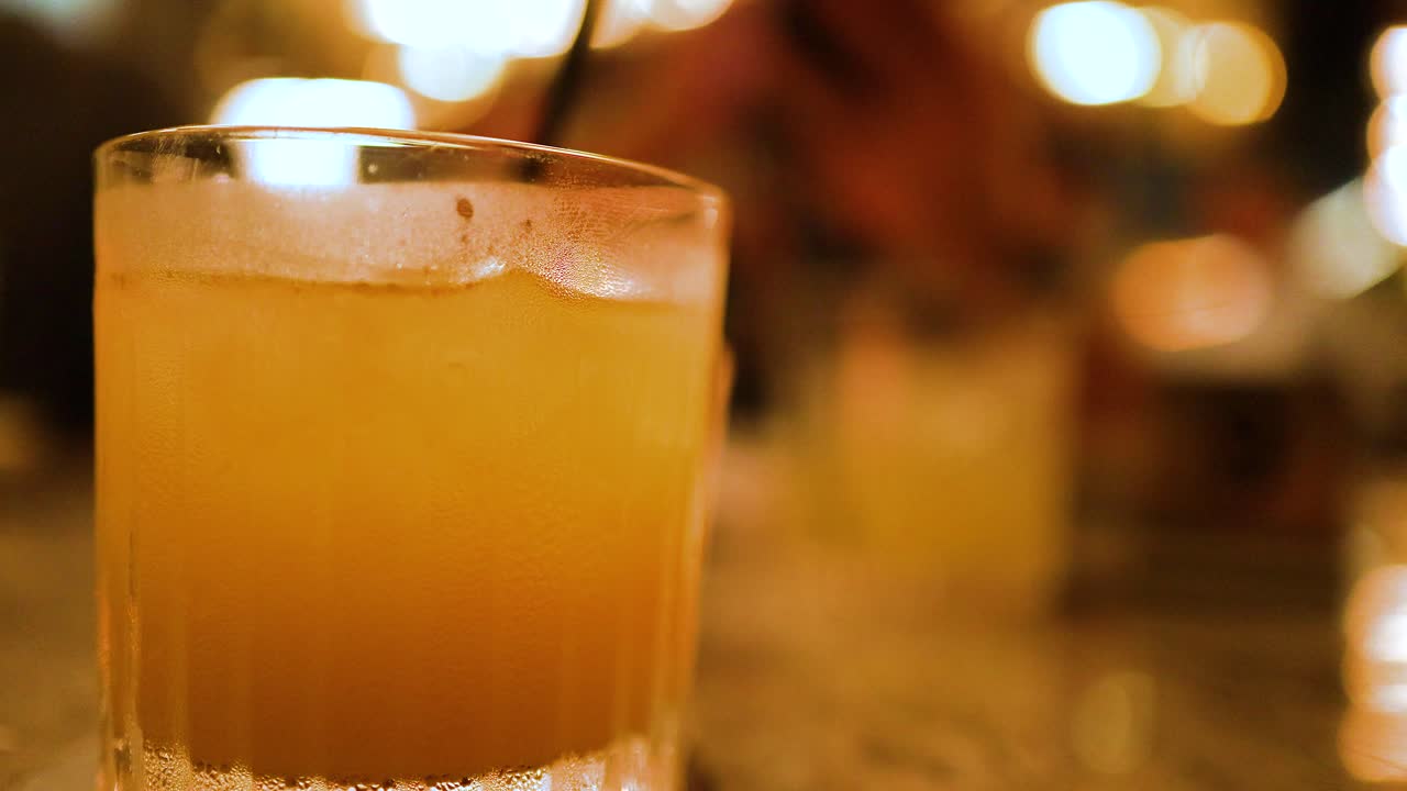 A close-up of a cocktail glass in a warmly lit bar, capturing the vibrant ambiance and social atmosphere