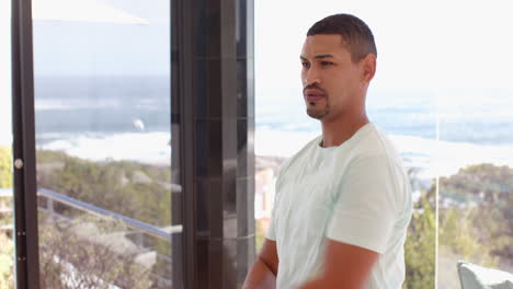 stretching arm, man standing by window with ocean view, wearing smartwatch