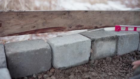 the man is using a level to ensure that the concrete block is properly aligned underneath the diy hot tub - close up