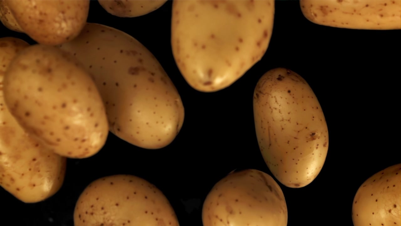 Patate crude che cadono al rallentatore su sfondo nero