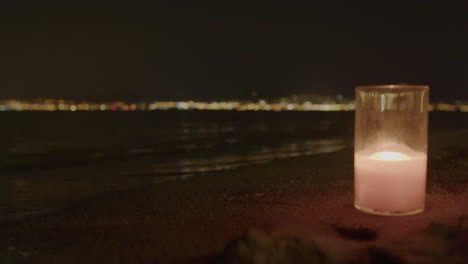 candle aglow with blurred city lights on beach