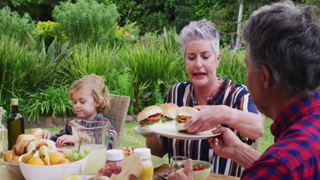 mujer caucásica mayor sonriente sirviendo a la familia teniendo una comida de celebración juntos en el jardín