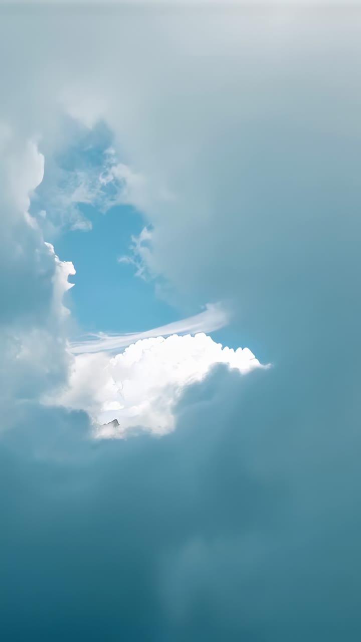 Vertical video: Shifting winds pulling clouds apart high above, revealing cumulus, contrail, peaks