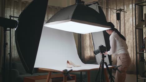 asian female photographer adjusting light equipment to get good illumination on women's shoes while taking photos of the products in home studio