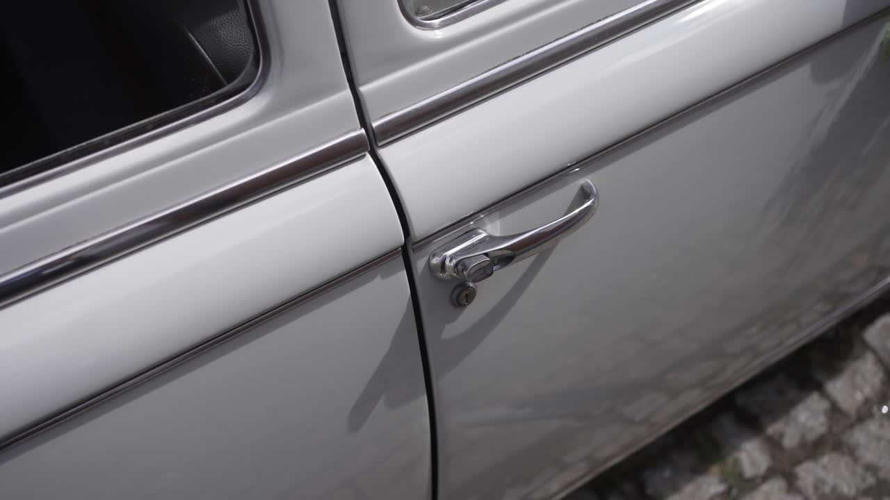 detail of silver vintage car door and chrome handle on cobblestone street