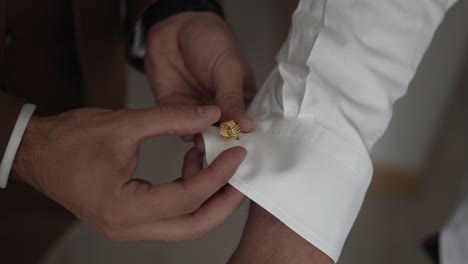 close up of gold cufflink being fastened on a white shirt during preparation