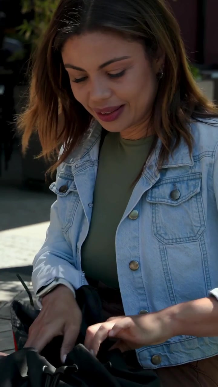 Video verticale: Donna in giacca di jeans che cerca dopo un tocco, frugando nella borsa nera in piazza, e poi se ne va