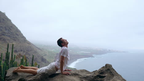 equilibrado en el borde de un acantilado, el hombre se involucra en una postura de perro, mirando hacia el océano, mientras respira el aire del mar como parte de su viaje de yoga a través de las islas