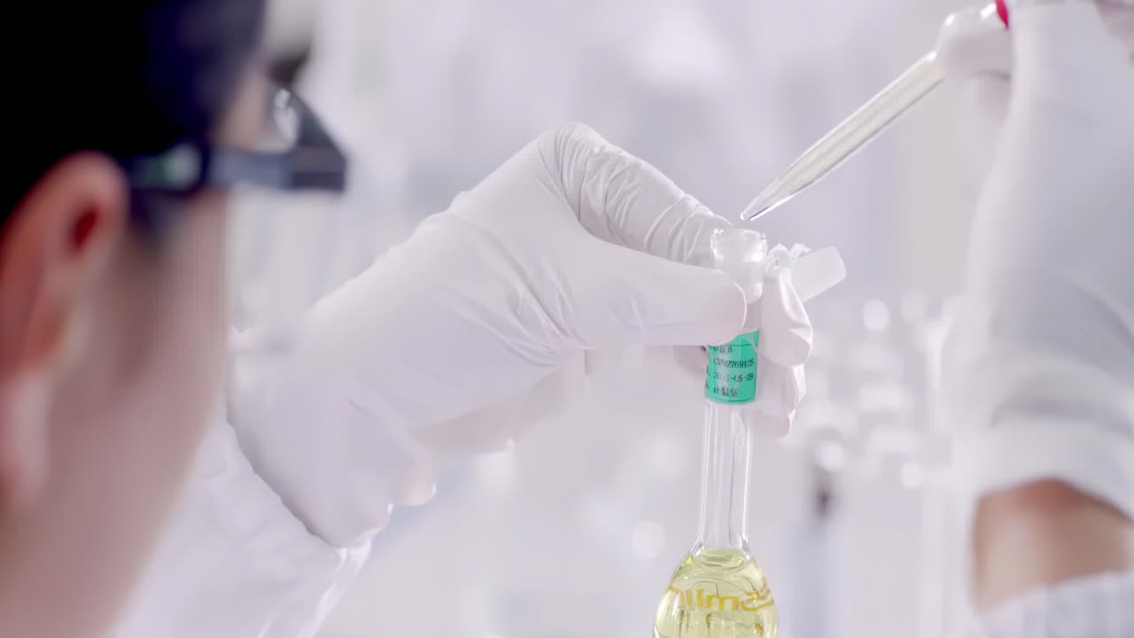 Medical Scientist or researcher in lab coats wearing safety glasses goggles dropper and chemical or test sample in beaker or test tubes working in biotechnology laboratory