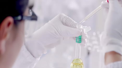 medical scientist or researcher in lab coats wearing safety glasses goggles dropper and chemical or test sample in beaker or test tubes working in biotechnology laboratory