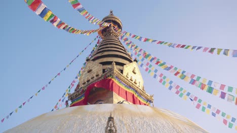 view of the beautiful swayambhunath stupa or monkey temple with colorful prayer flags with blue sky on the background. - panning up
