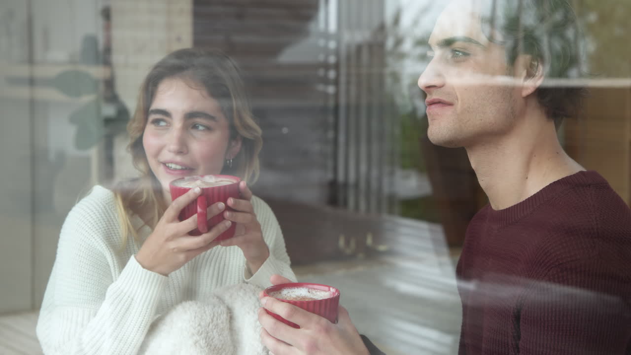 Christmas time, Couple enjoying hot cocoa together, gazing out window at home