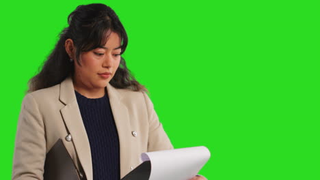 Close-Up-Studio-Portrait-Of-Female-Teacher-Or-Businesswoman-Standing-Against-Green-Screen-Looking-At-Clipboard-1