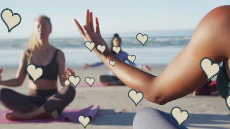 animation of yellow hearts over women practicing yoga on beach