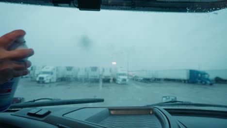 hand spraying cleaner on the inside windshield of a vehicle