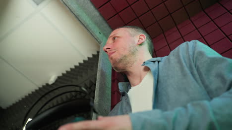 a man in a blue shirt and white inner receives headphones, poised in a vibrant, soundproof studio with a focused expression